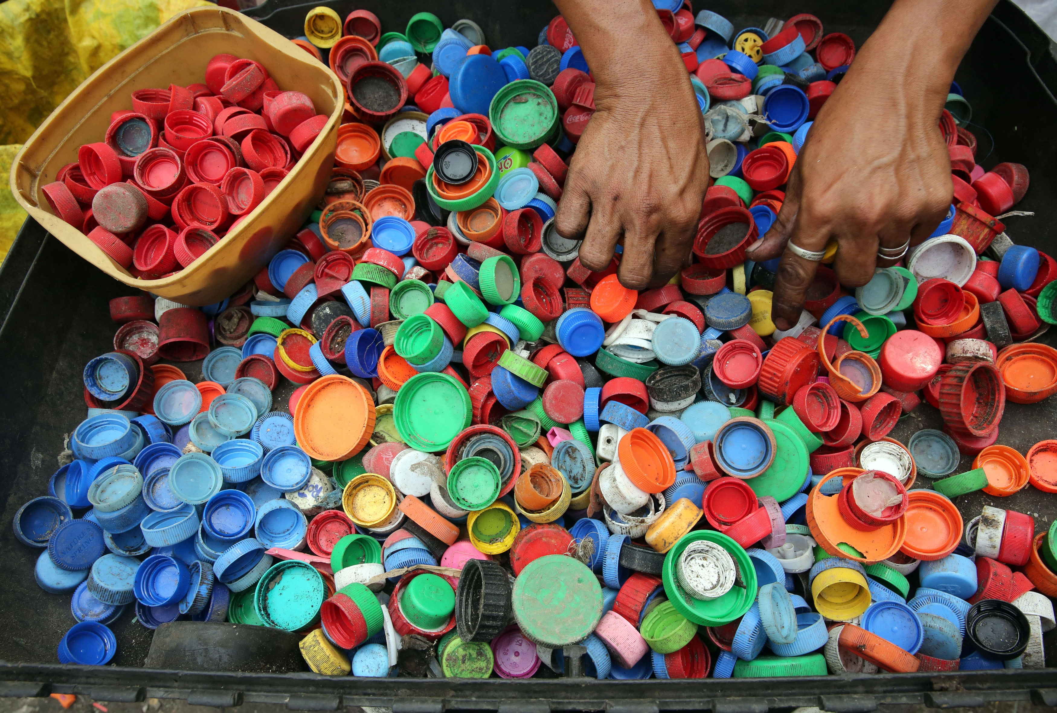 Sortare capace colorate, simbolizand sortarea selectiva in reciclare maini care sorteaza capace colorate de peturi
